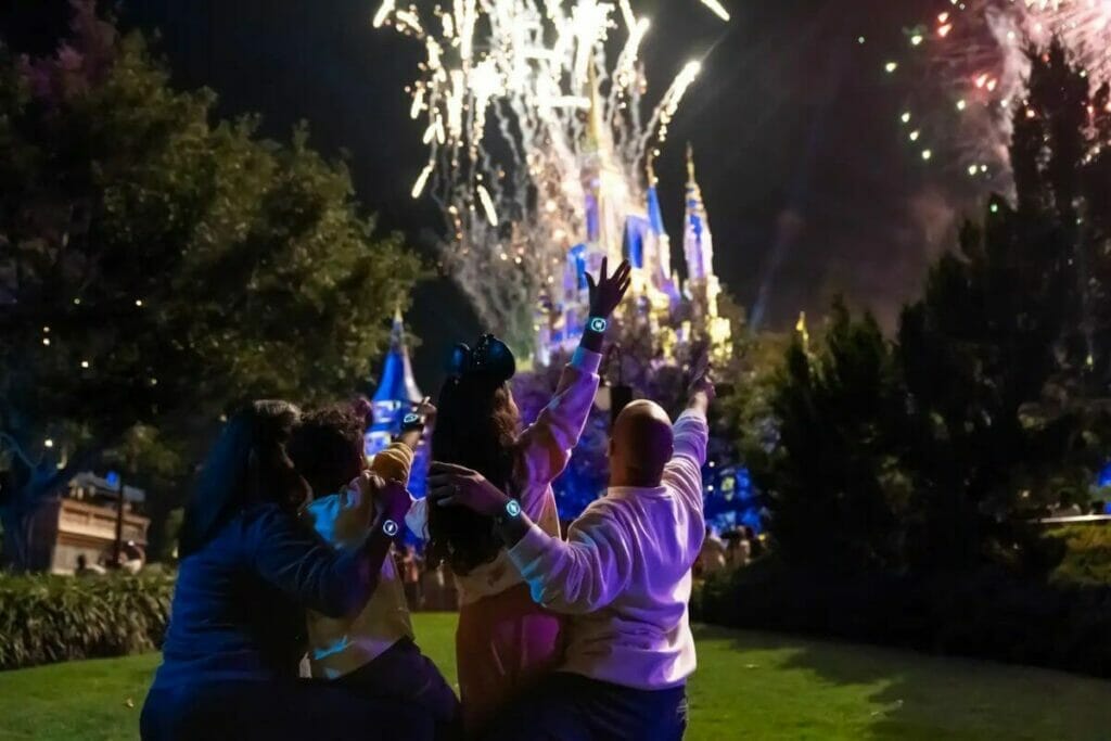 Family enjoying fireworks in front of Cinderella Castle while their Magic Bands light up on their wrists.