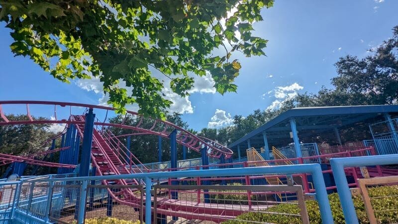 Peering out at Elmo's Choo Choo Train;s purple coaster track from under a tree on a bright day in Seaworld Orlando