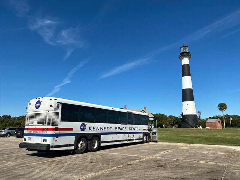 A Kennedy Space Center tour bus outside the Cape Canaveral Lighthouse under clear blue skies
