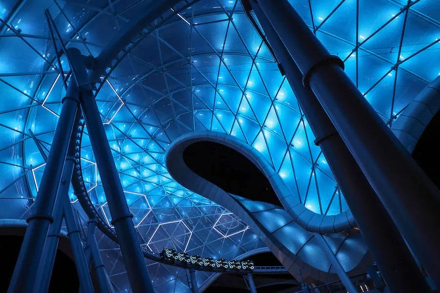 A Tron Lightcycle circles track under the lighting conduit lit in a blue glow at night