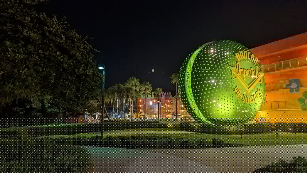 Looking towards Pop Century's amin pool at night with an oversized green yo yo lit in the darkness