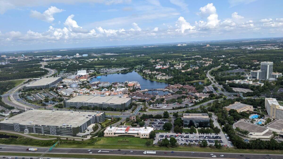 A birds eye view flying over Disney Springs with Walt Disney World in the background.