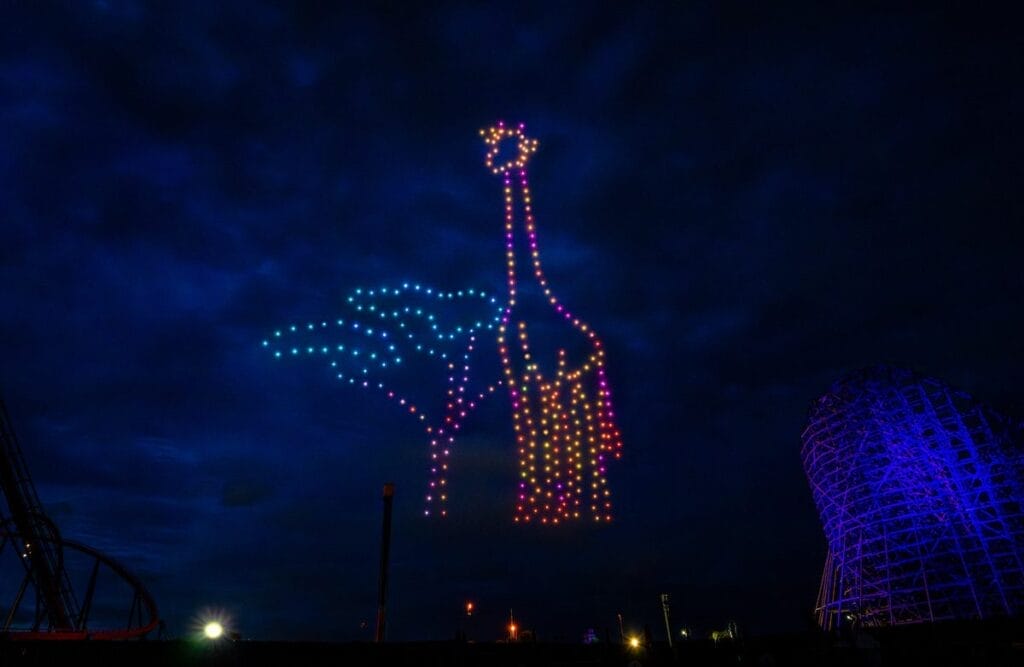 Drones lighting up the night sky beside Iron Gwazi in the shape of a giraffe and a tree